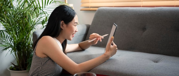 Heureuse femme se relaxant dans le salon et utilisant une tablette numérique