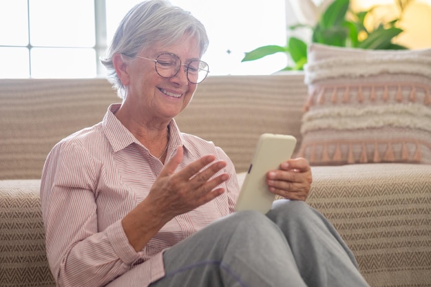 Heureuse femme senior agréable relaxante assise sur le sol tenant un smartphone dans les mains Une femme mûre souriante discutant sur les réseaux sociaux en regardant des vidéos amusantes à l'aide d'applications mobiles à la maison