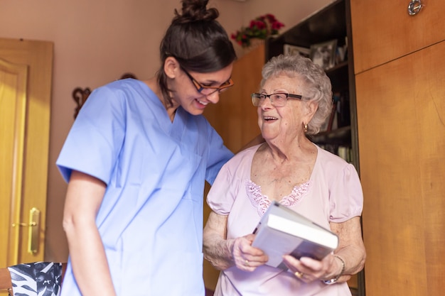 Heureuse femme senior avec son soignant à la maison, tenant un livre et souriant