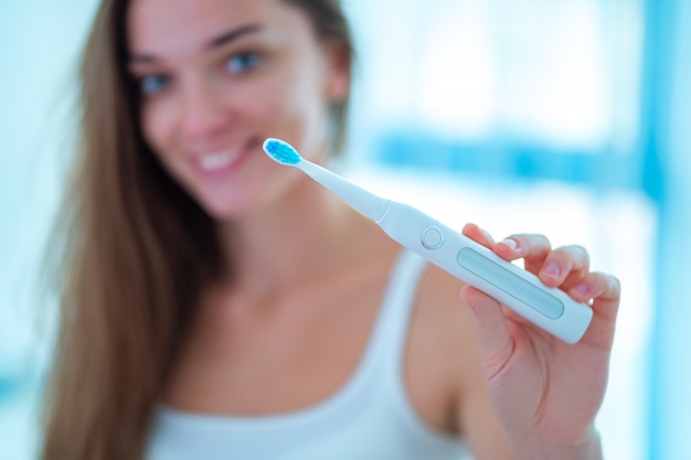 Heureuse femme souriante en bonne santé avec une brosse électrique à ultrasons dans la salle de bain à la maison. Hygiène dentaire et soins dentaires