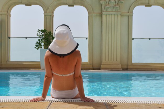 Heureuse femme souriante avec chapeau et lunettes de soleil dans la piscine du complexe tropical