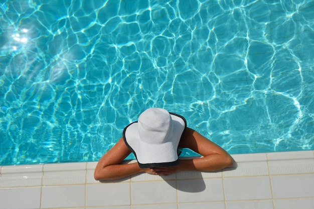 Heureuse femme souriante avec chapeau et lunettes de soleil dans la piscine du complexe tropical