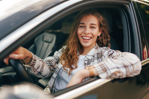 Photo heureuse femme souriante à l'intérieur d'une voiture conduisant dans la rue