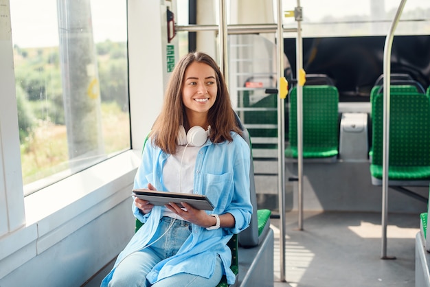 Heureuse femme souriante lit une tablette ou un ebook dans un tramway ou un métro moderne. Jolie fille monte pour travailler dans les transports publics.