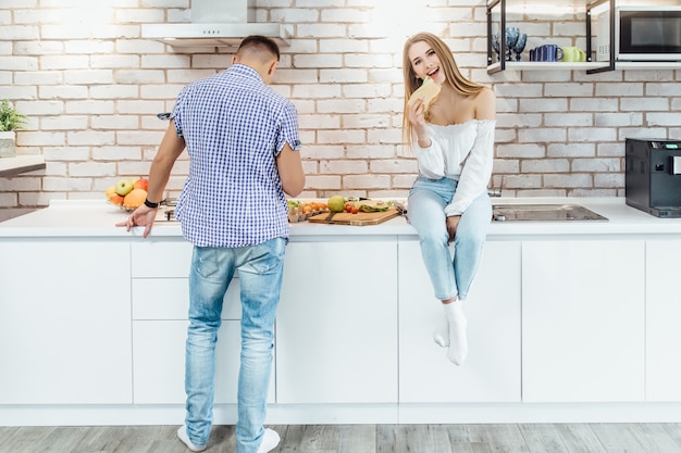 Heureuse femme souriante manger un sandwich pendant que son mari prépare manger