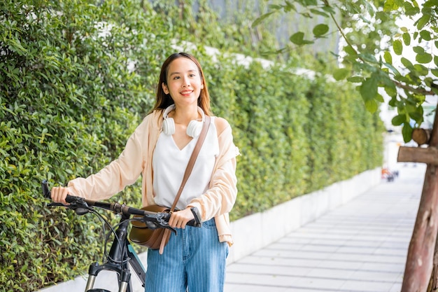 Heureuse femme souriante marchant dans la rue avec son vélo sur la route de la ville