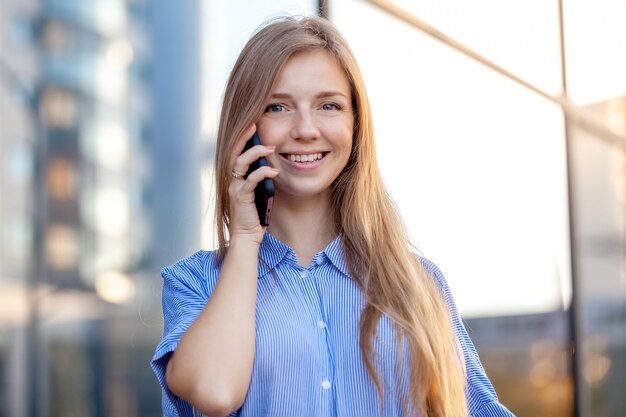 Heureuse femme souriante parlant au téléphone mobile et au bureau opposé