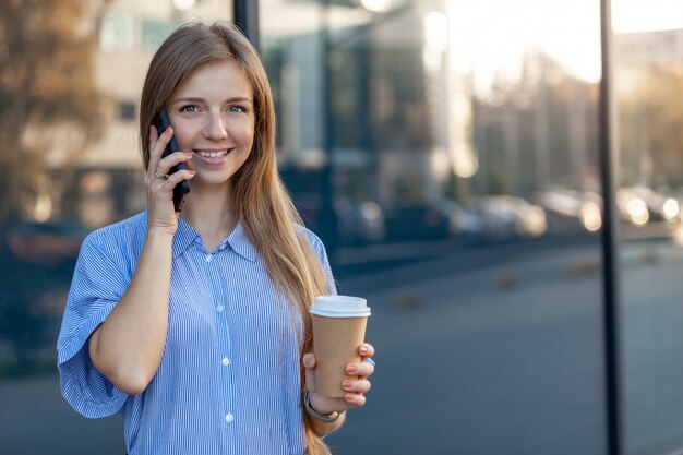 Heureuse femme souriante, parlant au téléphone mobile, tenant un café à emporter