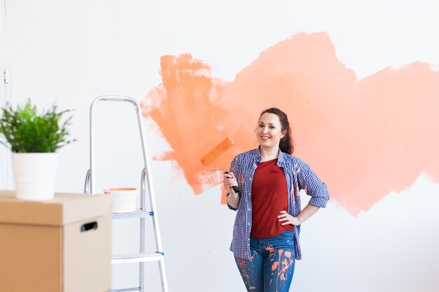 Heureuse femme souriante peinture mur intérieur de la nouvelle maison. Redécoration, rénovation, réparation d'appartement