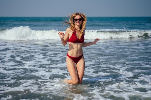 Heureuse femme souriante et s'amusant à la plage Portrait d'été d'une jeune belle fille en bikini rouge