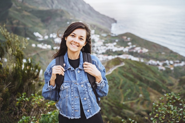 Heureuse femme souriante avec sac à dos sur l'océan et les montagnes. Concept de voyage et de style de vie