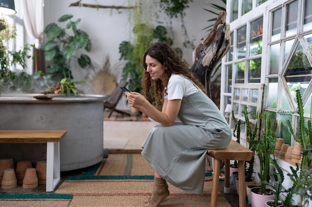 Heureuse femme souriante se détendre dans le jardin de la maison à l'aide d'un smartphone discutant sur les réseaux sociaux avec un ami