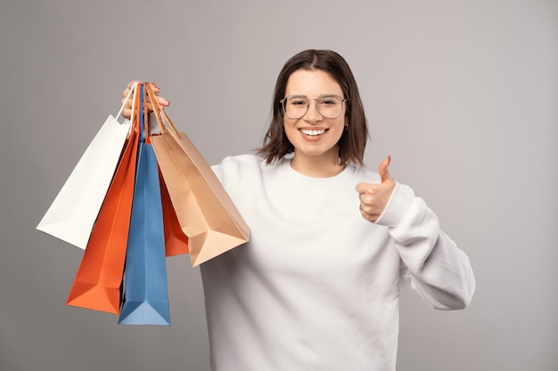 Heureuse femme souriante tient des sacs à provisions et le pouce vers le haut