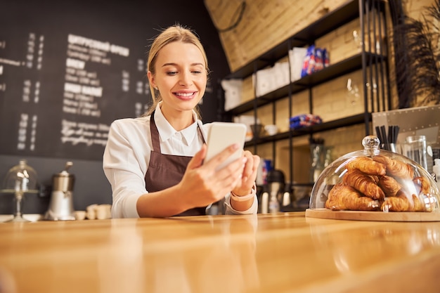 Heureuse femme souriante en uniforme en regardant le téléphone portable à écran