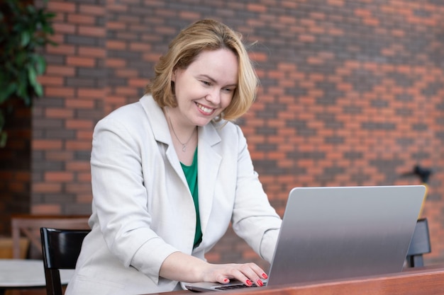 Heureuse femme souriante utilisant une application sur un ordinateur portable numérique dans un café de rue