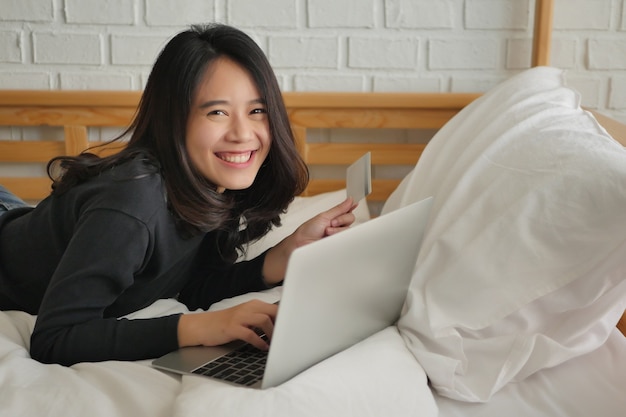 Heureuse femme souriante utilisant un ordinateur portable et une carte de crédit, concept de magasinage en ligne