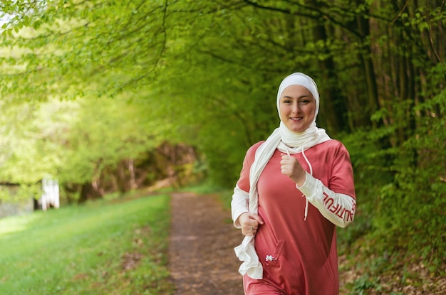 Heureuse femme sportive musulmane en hijab trail running en plein air dans le parc d'été