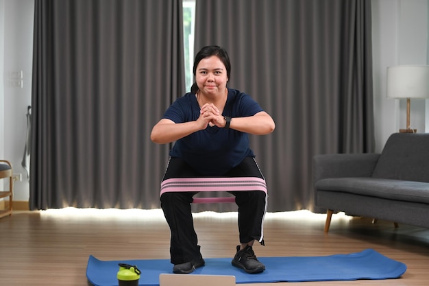 Heureuse femme en surpoids faisant de l'exercice avec un élastique à la maison