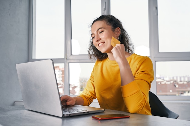 Heureuse femme tenant une carte de crédit et utilisant un ordinateur portable pour acheter en ligne