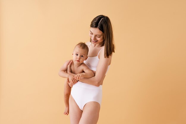 Heureuse femme tenant son bébé sur fond coloré - Jeune femme portant des sous-vêtements prenant soin de son petit fils - Concept de grossesse, de maternité, de personnes et d'attentes