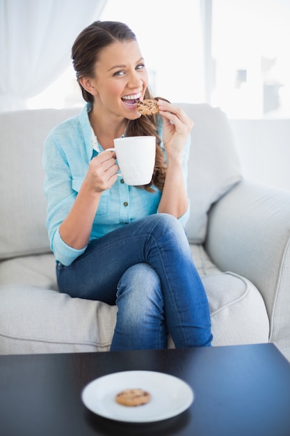Heureuse femme tenant une tasse de café en train de manger des biscuits