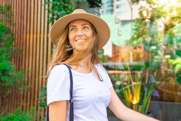 Heureuse femme touriste marchant dans la rue avec un chapeau pendant les vacances d'été profitant de voyager en vacances