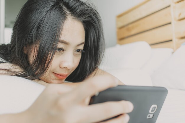 Heureuse femme utilise un smartphone et se détend sur son lit.