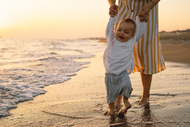 Heureuse fête des mères Belle mère et bébé jouent sur la plage Maman et son enfant profitant ensemble du coucher du soleil Une mère célibataire aimante embrasse un petit fils mignon