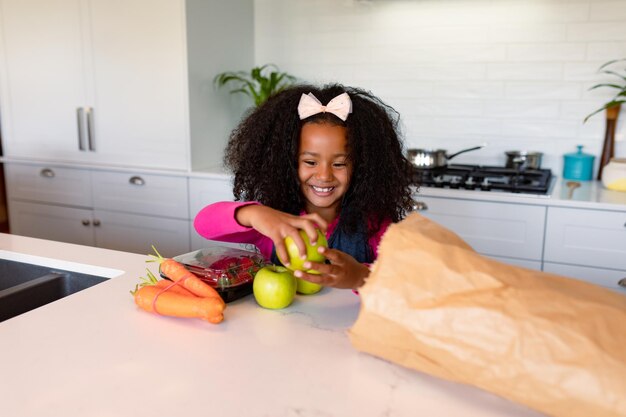 Heureuse fille afro-américaine déballant les courses dans la cuisine