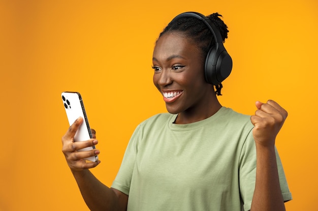 Heureuse fille afro-américaine souriante à l'aide de son smartphone en studio jaune