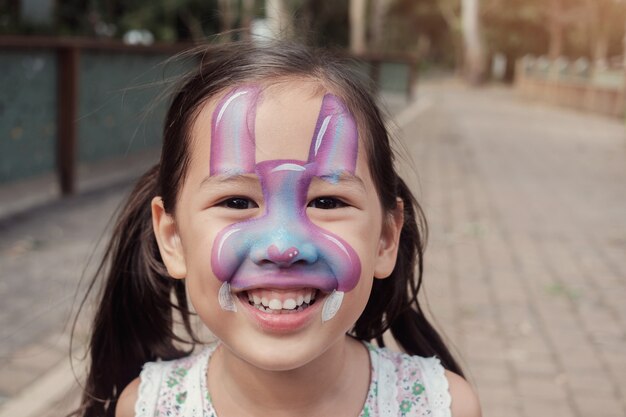 Heureuse fille asiatique multiculturelle avec la peinture de visage lapin lapin