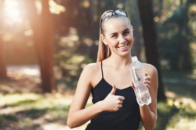 Heureuse fille athlétique buvant une bouteille d'eau à la récolte panoramique de la bannière du parc