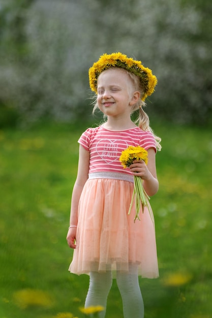 Photo heureuse fille blonde aux yeux fermés portant une couronne de pissenlit à l'extérieur enfant avec bouquet de pissenlits arrière-plan flou cadre vertical
