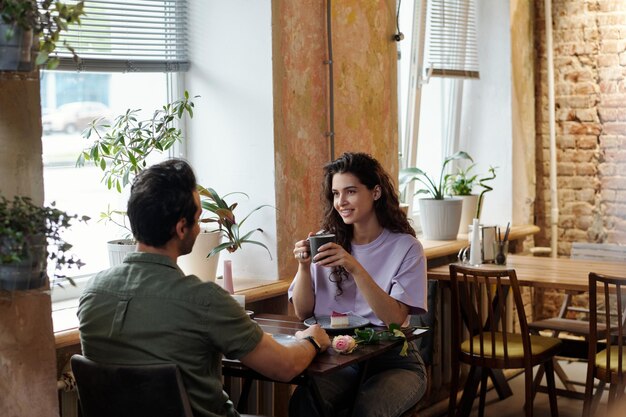 Heureuse fille brune avec une tasse de café et son petit ami en train de discuter