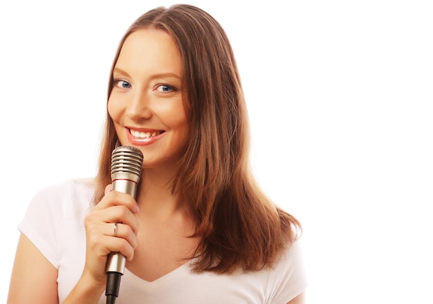 Heureuse fille chantant Beauté femme portant un t-shirt blanc avec microphone sur fond blanc