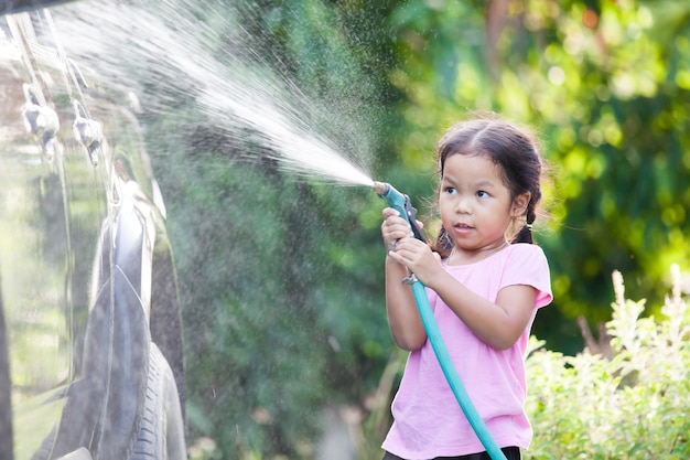 Heureuse fille enfant asiatique aide parent lavage voiture sur l&#39;eau éclaboussant avec la lumière du soleil