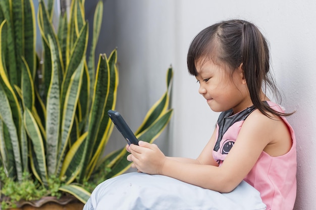 Photo heureuse fille enfant asiatique regardant et utilisant un téléphone intelligent