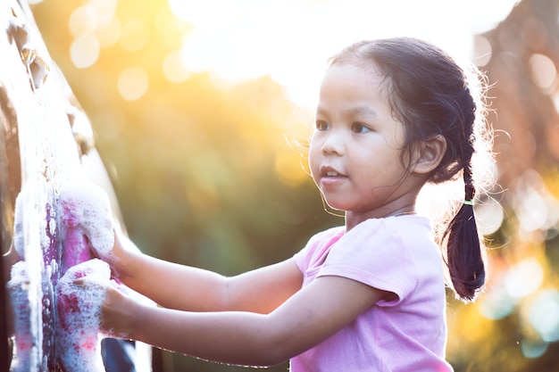 Heureuse fille enfant asiatique s&#39;amuser pour aider les parents à laver la voiture avec la lumière du soleil