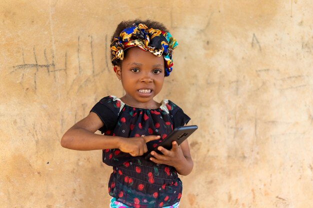 Heureuse fille enfant souriante regardant dans son téléphone portable à l'extérieur en été