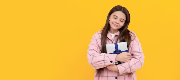 Heureuse fille enfant sourire avec les yeux fermés tenant une boîte-cadeau fond jaune présent Adolescente avec affiche horizontale de cadeau d'anniversaire En-tête de bannière avec espace de copie