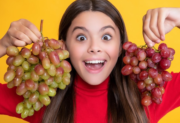 Heureuse fille étonnée tenir une grappe de raisin sur fond jaune