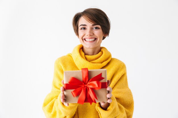 Heureuse fille gaie portant un chandail à capuchon debout isolé sur blanc, tenant une boîte-cadeau