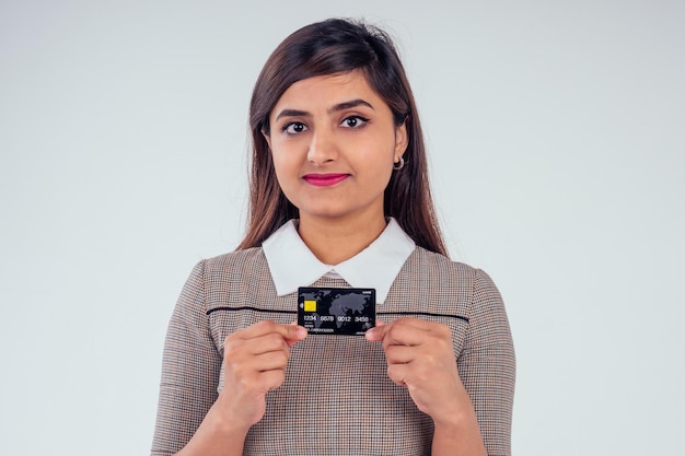 Heureuse fille indienne tenant une carte de crédit sur fond blanc de studio.