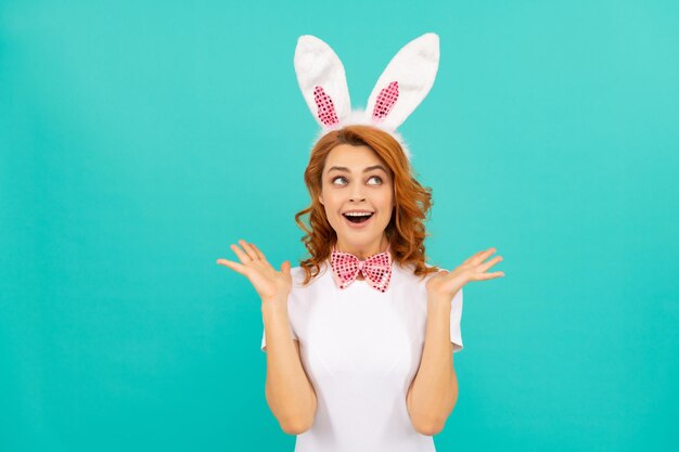 Heureuse fille de pâques étonnée dans les oreilles de lapin et noeud papillon sur fond bleu