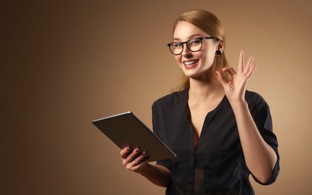 Heureuse fille professionnelle portant des lunettes et tenant la tablette isolée sur le mur brun