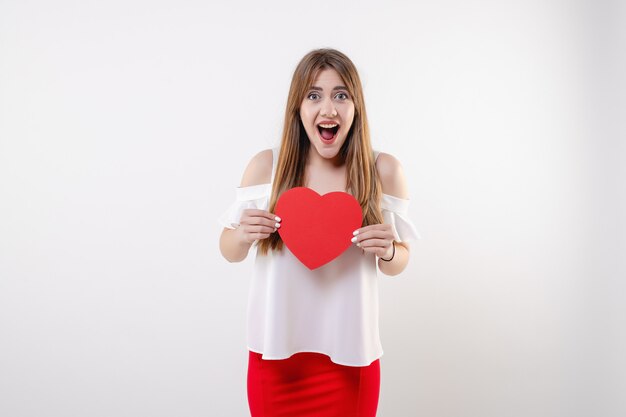 Heureuse fille qui crie avec carte de Saint Valentin en forme de coeur rouge isolé