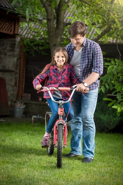 Heureuse fille souriante apprenant à faire du vélo avec son père au parc