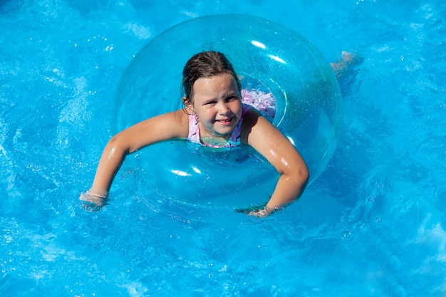 Heureuse fille souriante flottant dans un cercle gonflable transparent pour la sécurité sur l'eau dans le bleu c...