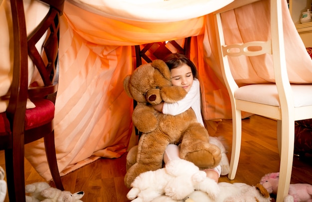 Heureuse fille souriante en pyjama étreignant l'ours en peluche à la maison selfmade