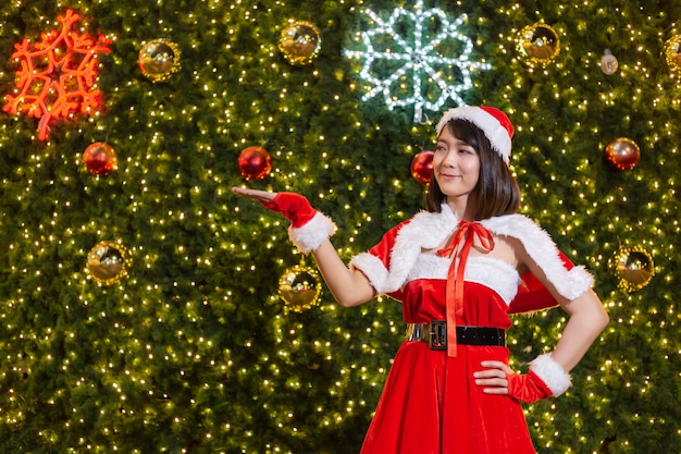 Heureuse fille souriante de Santa est mignonne en costume rouge avec la célébration de fond de sapin de Noël